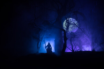 Death with a scythe in the dark misty forest. Woman horror ghost holding reaper in forest,...