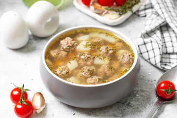 Vegetable soup with meatballs in a ceramic plate on a light background closeup