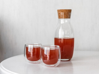 Red drink in elegant carafe and two glass on white table. Bright juice in light background. Compote...