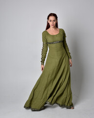 full length portrait of red haired girl wearing celtic, green medieval gown. Standing pose isolated against a studio background.