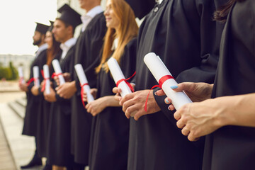 Close up of row of students in black robes standing with traditional rolled up diplomas in hands at...