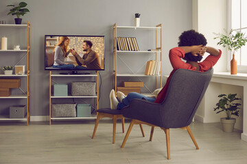 Woman relaxing in chair at home and enjoying television soap opera with a happy ending. Young lady sitting in comfortable armchair in living-room and watching romantic series or reality show on TV