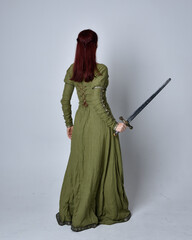 full length portrait of red haired girl wearing celtic, green medieval gown. Standing pose, holding...