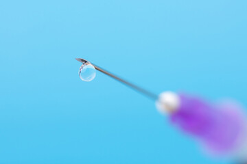 Macro shot of a needle of a syringe with a drop on its end. Symbol of vaccination, medicine, treatment