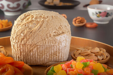 Sunflower halva sprinkled on a wooden dish with pistachios, peanuts, dried apricots, candied fruit syrup and on a dark background. Eastern sweets. Close-up