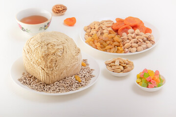 Sunflower halva on a white plate against the background of pistachios, peanuts, candied fruits, raisins, dried apricots and Asian cups for tea on a white table. Eastern sweets.