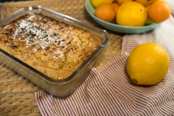 a delicious lemon shortbread pie in a glass baking dish and on a wooden board lies on a towel with ripe yellow and orange citrus fruits on a blue background