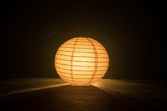 Beautiful paper lantern glowing on wooden table in dark.