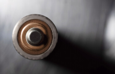 Overhead shot of a battery on a metallic gray background, with space on the right side for text. Macrophotography.