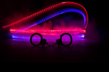 Police raid at night and you are under arrest concept. Silhouette of handcuffs with police car on...