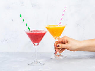 Two martini glasses of sicilian orange and tangerine smoothie with straws on grey background.