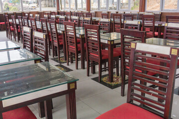 Dining table set up indoor with empty wooden chairs and glass tables, prepared for an event