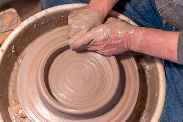 close up on male hands working on a potters wheel to make a bowl