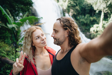 Happy couple taking selfie portrait at tropical waterfall in Thailand