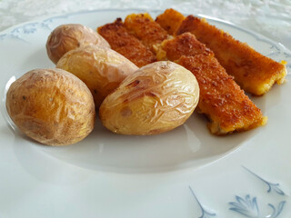 Jacket potatoes with fish sticks on a white plate. Food, close up.