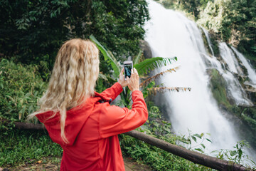 A woman wearing a red jacket make photo of a waterfall