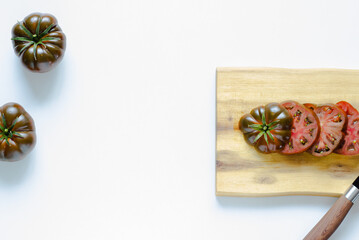 Two whole dark red tomatoes and one cut dark red tomato on wooden cutting board and white background; cutting vegetables