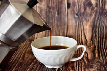 coffee pours from the coffee maker into a white porcelain cup 