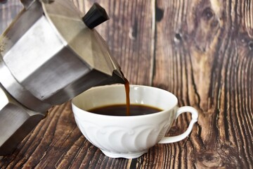 coffee pours from the coffee maker into a white porcelain cup 