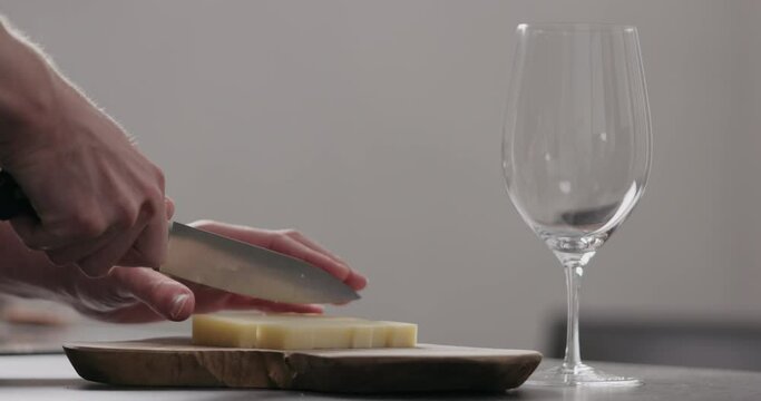 Slow motion man hands cutting vintage cheese on oliveboard with wine glass