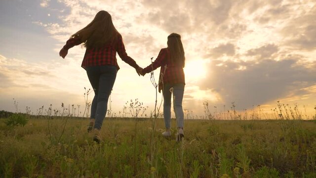 Two happy teenage girls run at sunset together. Girls run hand in hand in the park. Silhouette of children running at sunset in the park.