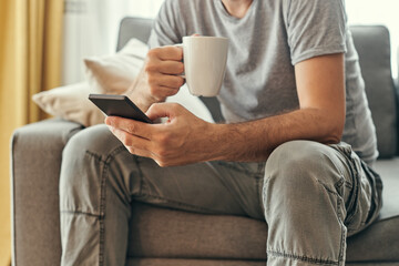 Man drinking coffee and using mobile phone at home