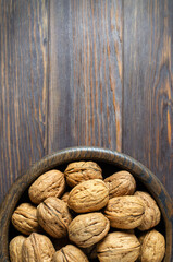 Walnuts in a plate on a brown wooden background. Nuts are a source of vegetable protein. Copy space. Flat top view.