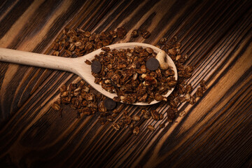 Chocolate granola cereal with nuts in a wooden spoon.