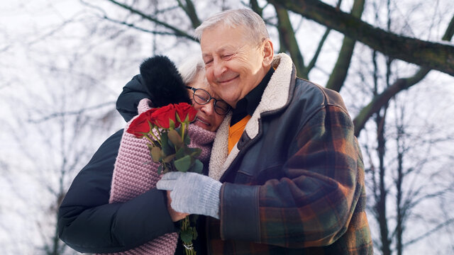 Dating at old ages. Happy elderly man giving bouquet of red roses to his wife. High quality photo