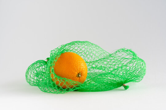 A single orange in a green net bag on white background with copy space, food shopping