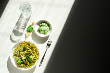 Green noodles with spinach and parmesan cheese in a white plate on a white table. Hard light and shadows. Healthy food. Basic ingredients. A place for text.