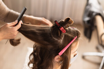 Fototapeta premium Hairdresser is preparing the girl hair style for photo shoots. Hairdresser to curl the hair in a beauty salon, barber shop. Reopening the hair salons after pandemic.