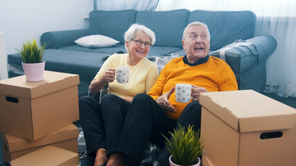 Happy retired couple relocating to new appartment. Drinking coffee surounded by cardboard boxes....