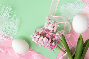 Two white egg, pink hyacinth flowers with pink ribbon on pastel green and pink colors. Happy Easter concept.