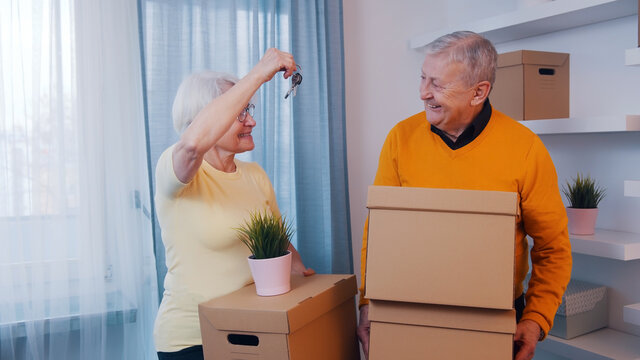  Woman holding house keys and man carrying cardboard boxes. Elderly couple buying new home. High quality photo