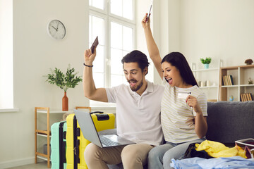 Vacation time. Emotional happy couple buy ticket sitting on couch using laptop looking at device screen screaming and making big open eyes and mouth received huge discounts for booking tour online