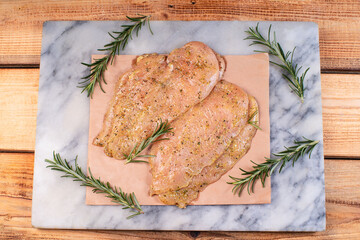 Sottilissime raw chicken fillet.Chicken fillet, thinly sliced, sottilissime marinated with various herbs on a plate on a marble cooking board.