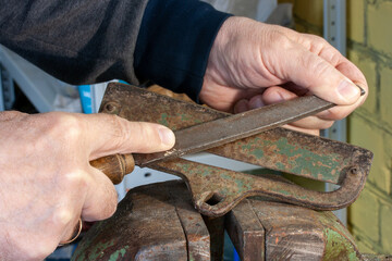 Sharpening the hoe knife with a file before spring work in the garden
