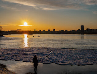 A girl on the shore at sunset is waiting for the fishermen. Winter shooting. Cityscape.