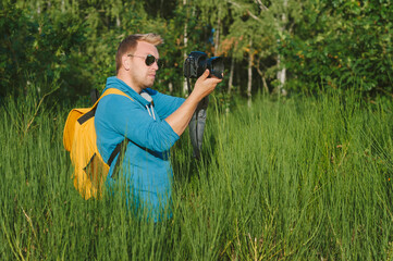 A man holds a professional photo-video camera in his hands. Against the backdrop of green nature and forest.