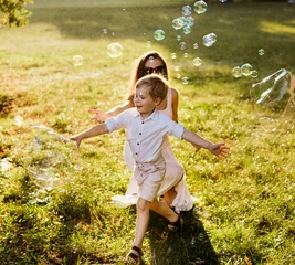 Foto op Aluminium Cheerful mother looking at her son chasing a soap bubble © konradbak