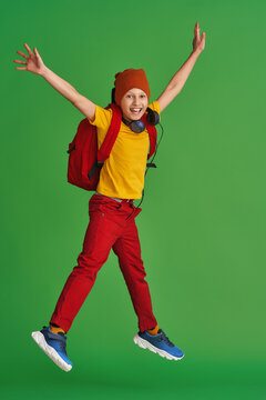 cheerful schoolboy in free-style clothes, headphones, backpack and books jumps on yellow background. Dynamic images go back to conceptual school. holidays begin. Back to school. boy is ready to learn