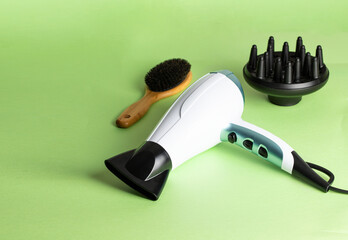 Different accessories for hair care and styling , Ionic hairdryer with  diffuser , natural wood brush on green background.