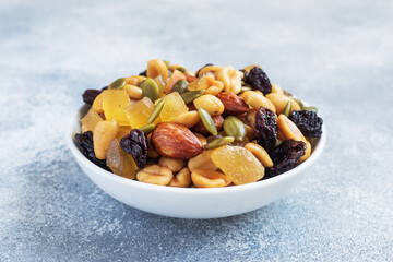 A mixture of nuts and dried fruits in a ceramic plate on a gray concrete background. Concept of healthy food.