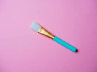 A blue cosmetic brush for applying face masks lies on a pink background. Cosmetic accessories