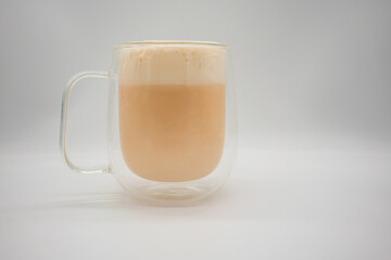 Hot Thai milk tea with milky foam sprinkle with cocoa power for decoration in double wall glass isolated on white