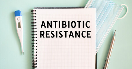 Notepad, medical mask, thermometer and pen on a blue background. ANTIBIOTIC RESISTANCE text in a notebook.