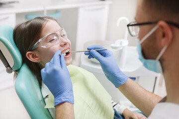 Fototapeta premium Adorable happy young girl smiling at her dentist during teeth treatment