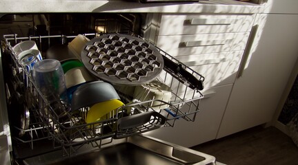 Opened dishwasher with clean plates, spoons is in the kitchen, close up view.