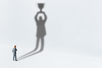 Comtemplating on business success, top performance, winner concept : Businessman looks his shadow raising a trophy cup on the wall, depicts scrutinizing on ways to race and achieve goals and win prize